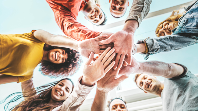Group of young adults putting there hands in the middle of the photo
